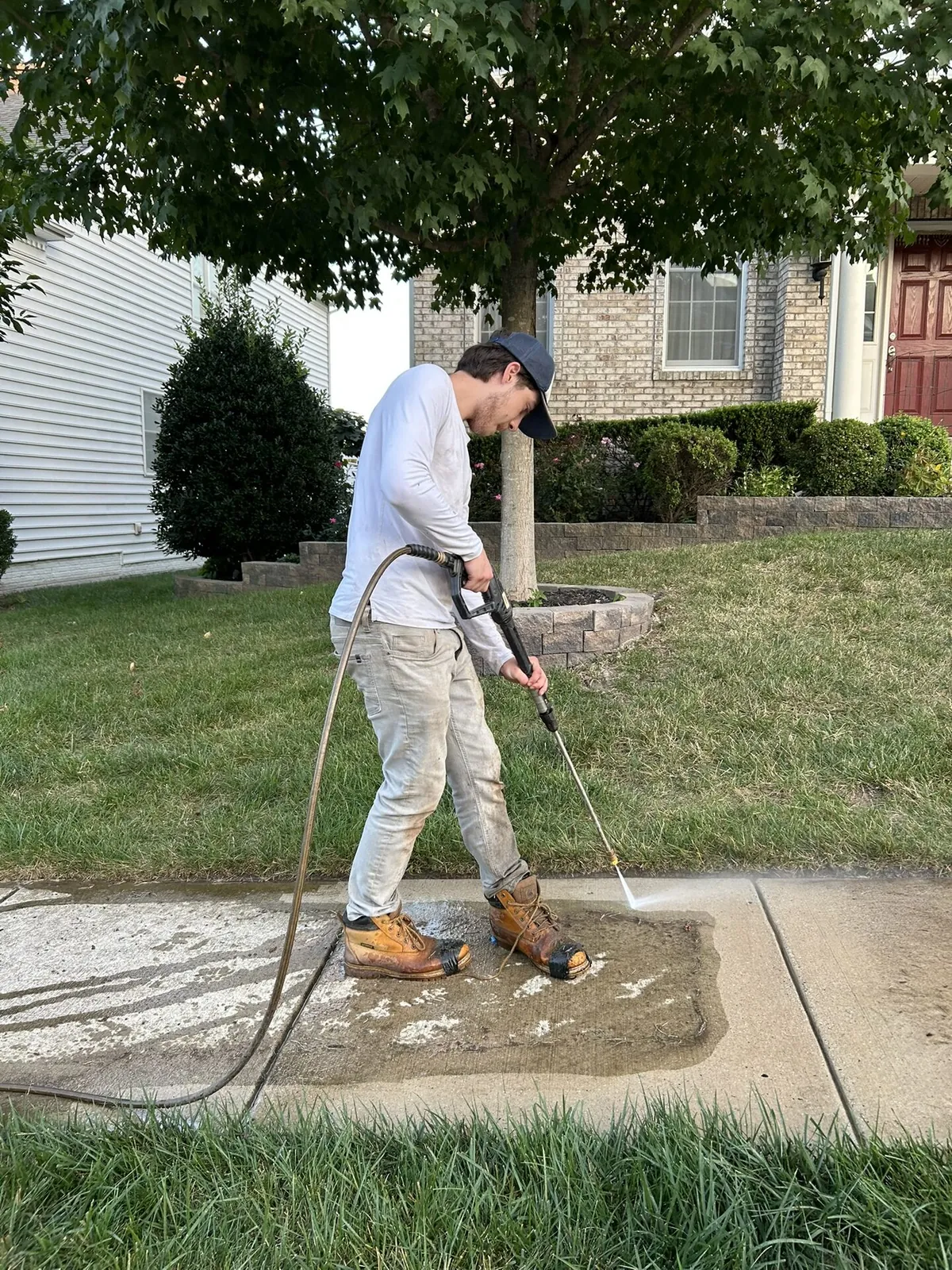 Crew member pressure washing sidewalk with green lawn